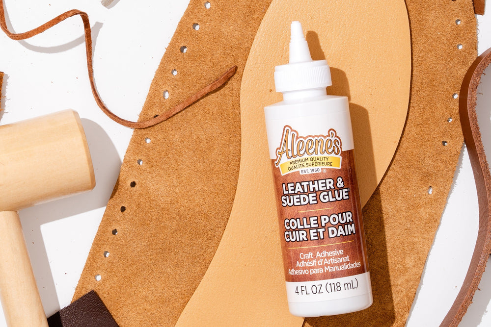 Aleene's leather and suede glue bottle on a white background with leather crafting tools.